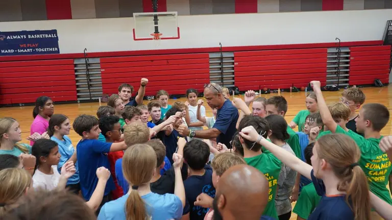 Coach V leading a huddle with young players at an Always Basketball youth camp.